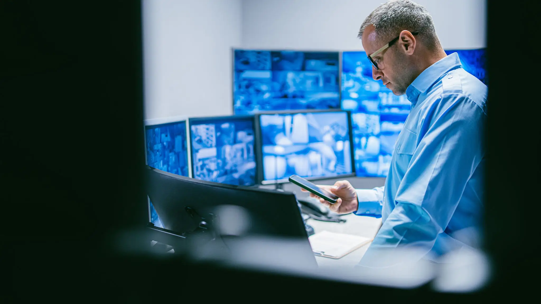 Security operator checking tablet with surveillance monitors